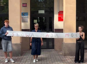 Uczniowie wraz z nauczycielem trzymający rolkę papieru z napisem słowa mają moc