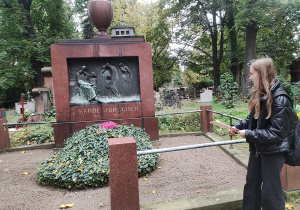 Uczennica prezentuje postać Karola Jonschera przy jego nagrobku na Starym Cmentarzu w Łodzi.