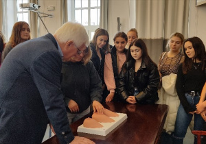 Uczennice stoją przy stole i pod kierunkiem profesora z Centrum Zdrowia Matki Polki w Łodzi uczą się na fantomach piersi wykrywania guzków nowotworowych