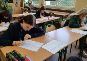Uczniowie siedzą w ławkach i rozwiązują zadanie z mapą Polski podczas II etapu eliminacji