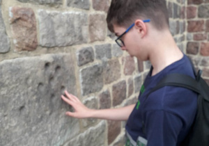 Uczeń szuka śladów diabła Boruty na murach kolegiaty w Tumie